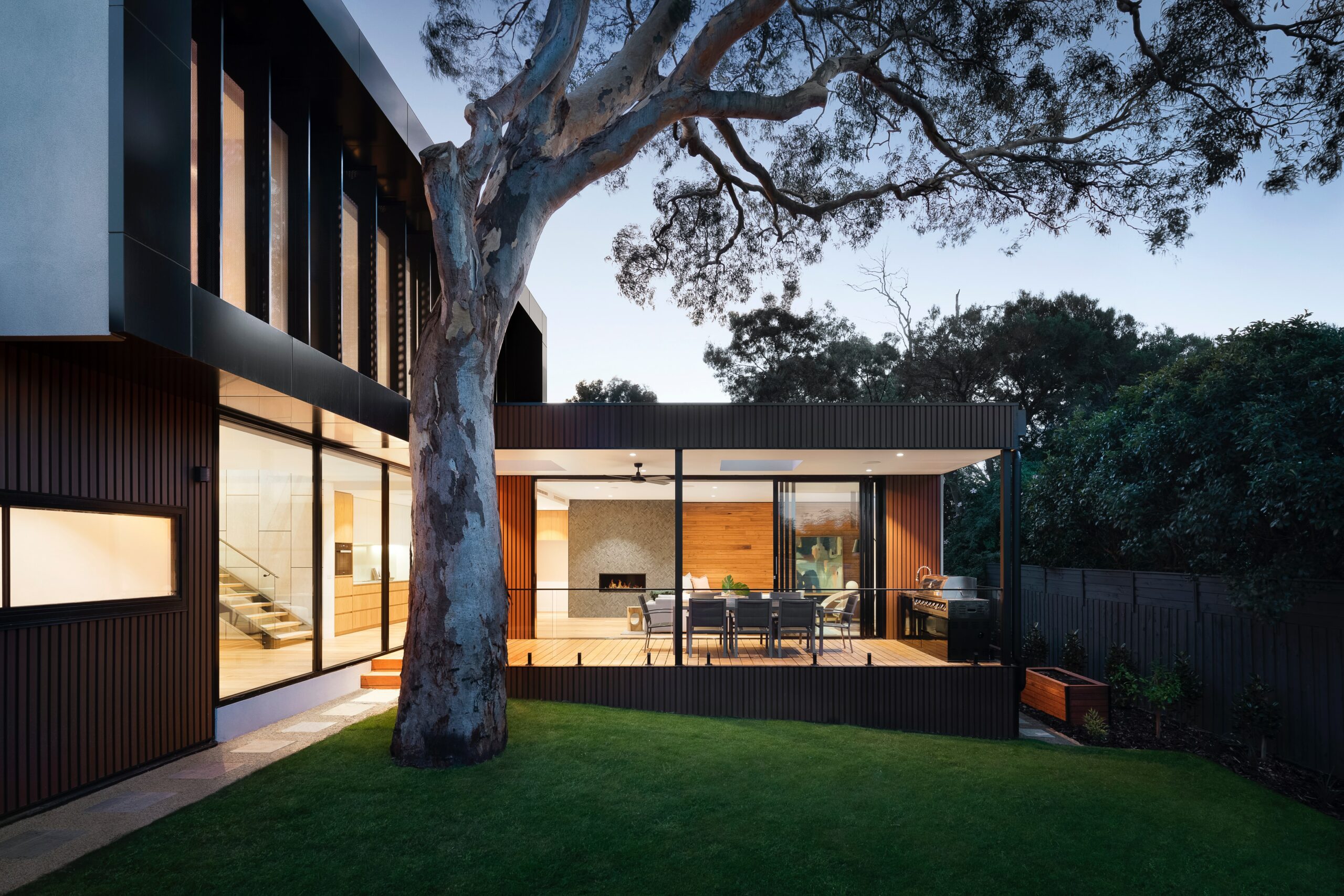 Modern home extension with large glass windows and a covered outdoor seating area, exemplifying a project that may fall under permitted development. The integration of the design with surrounding trees and garden suggests minimal disruption to the natural landscape.